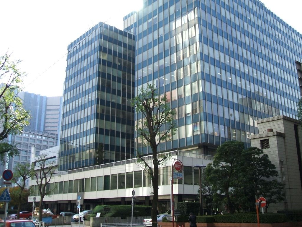 Two glass office blocks above a low podium on a tree-lined Ginza street