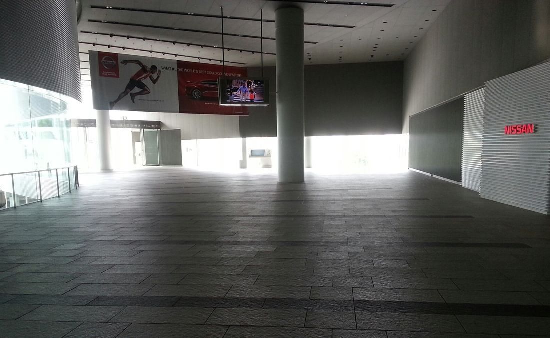 Nissan: Wide stone-paved public walkway under a high ceiling, open to daylight at the far end