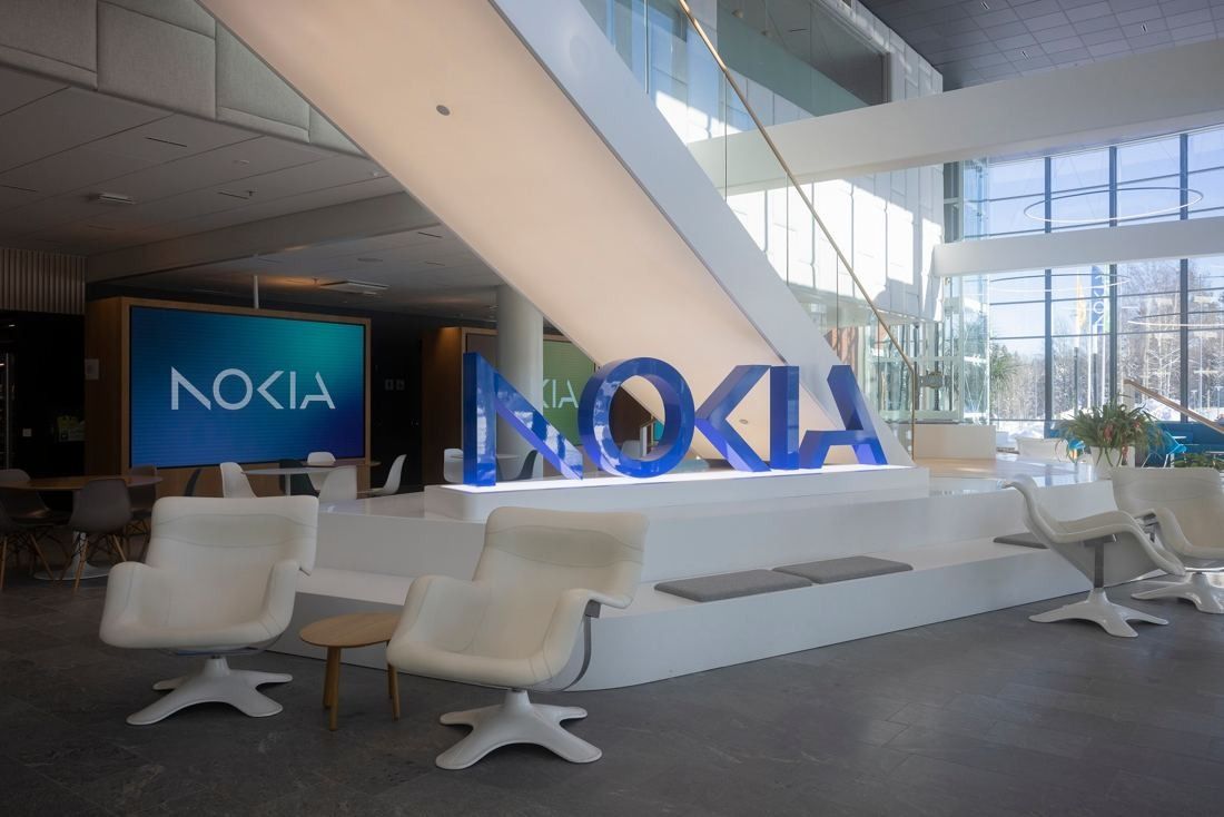 Nokia: Bright double-height lobby with large blue NOKIA letters on a white stepped platform, white lounge chairs and a staircase