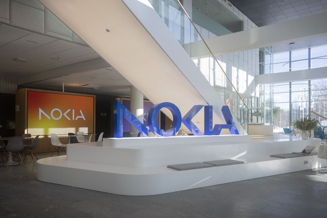 Nokia: Lobby with large blue NOKIA letters on a white platform under a staircase, an orange screen and café tables behind