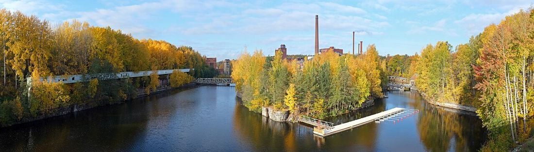 River with a wooded island in autumn colours and a factory chimney in the background