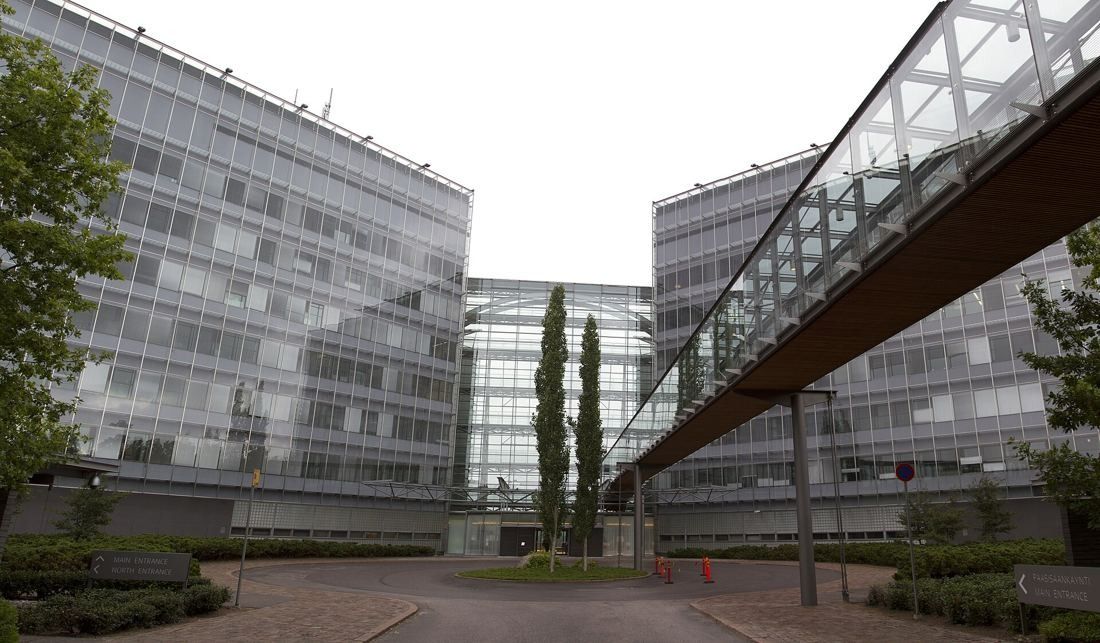 Two glass office wings joined by a glazed bridge over a paved entrance court
