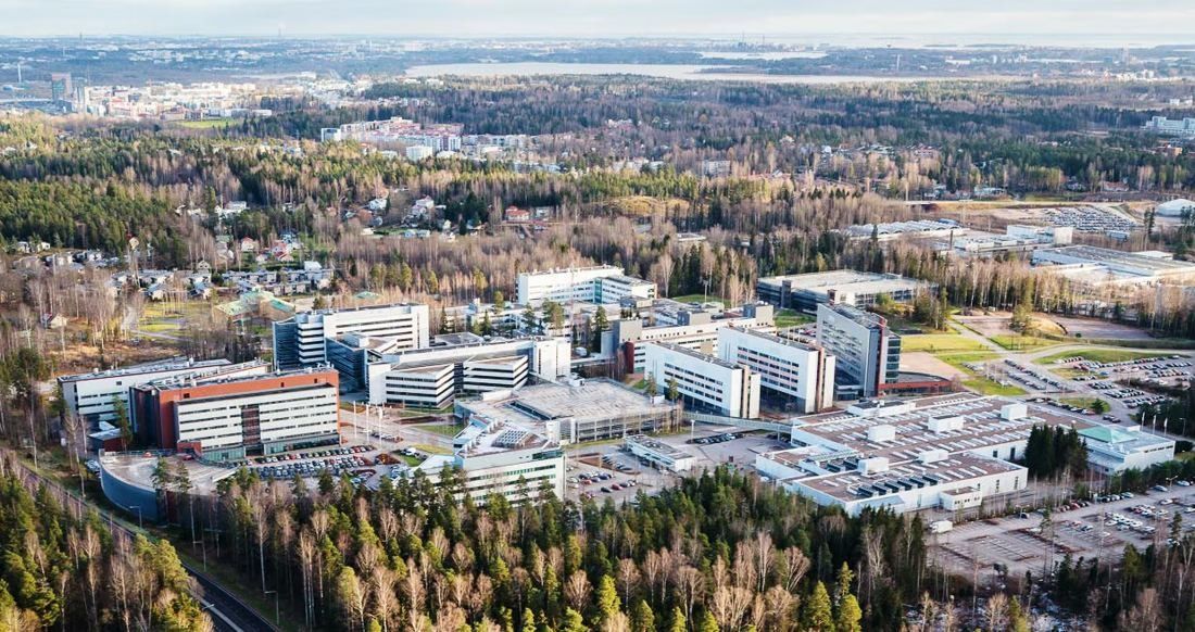 Nokia: Wide aerial view of a campus of office buildings set among forest, with the city beyond