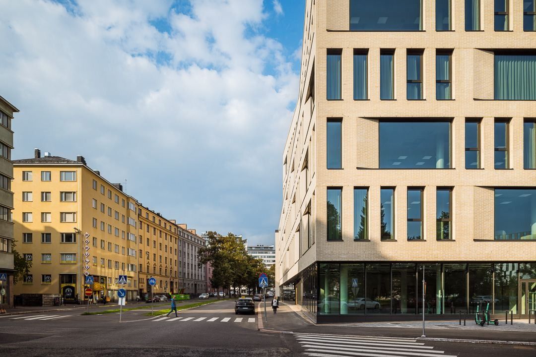 Nordea: Corner of the pale brick building with a glazed ground floor facing a street of yellow apartment blocks