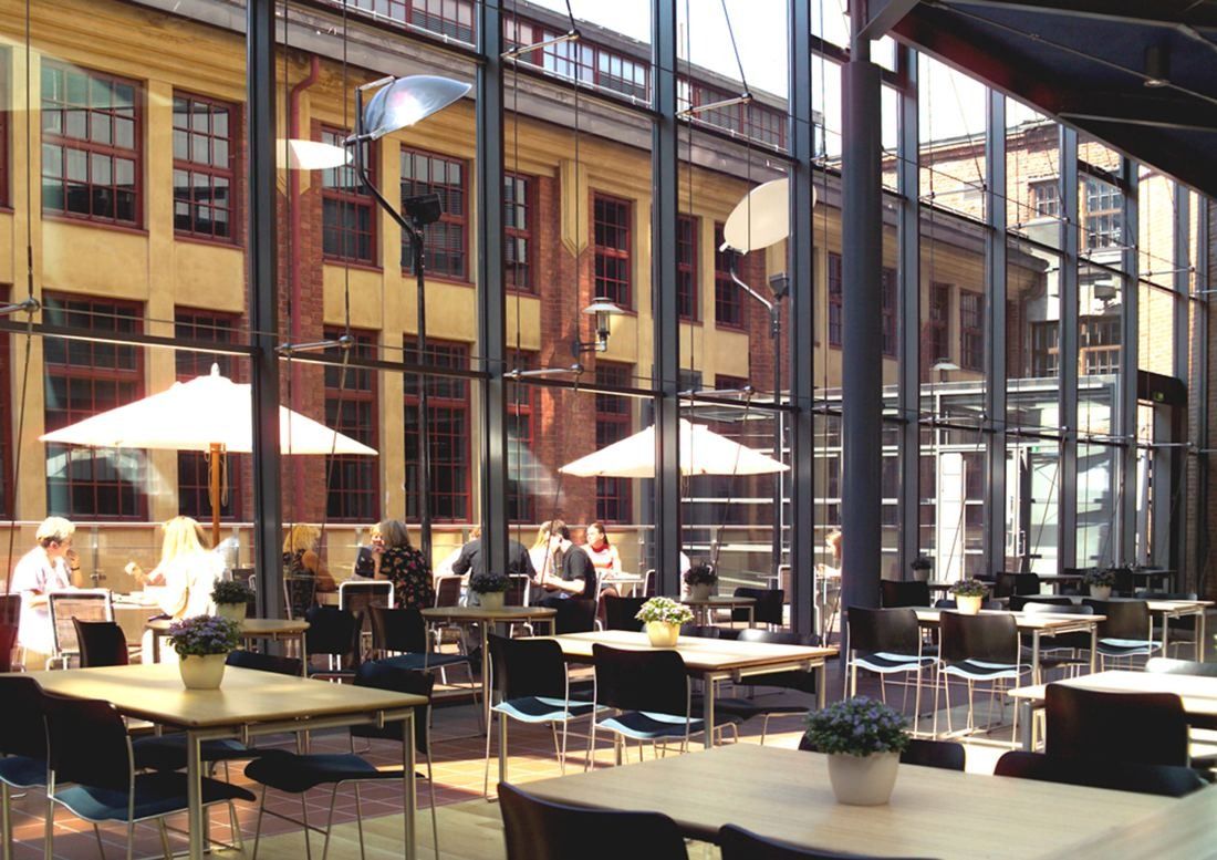 Nordea: Glass-roofed restaurant courtyard with tables, parasols and old brick factory facades behind