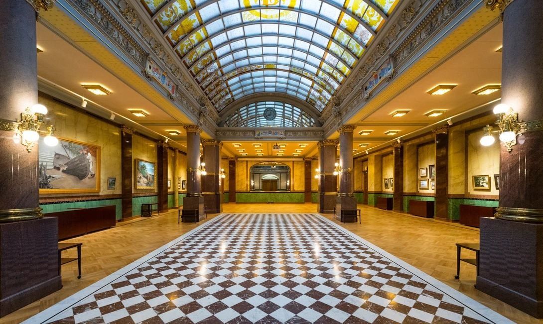Long banking hall with a glass barrel-vaulted ceiling, dark columns and a checkered floor