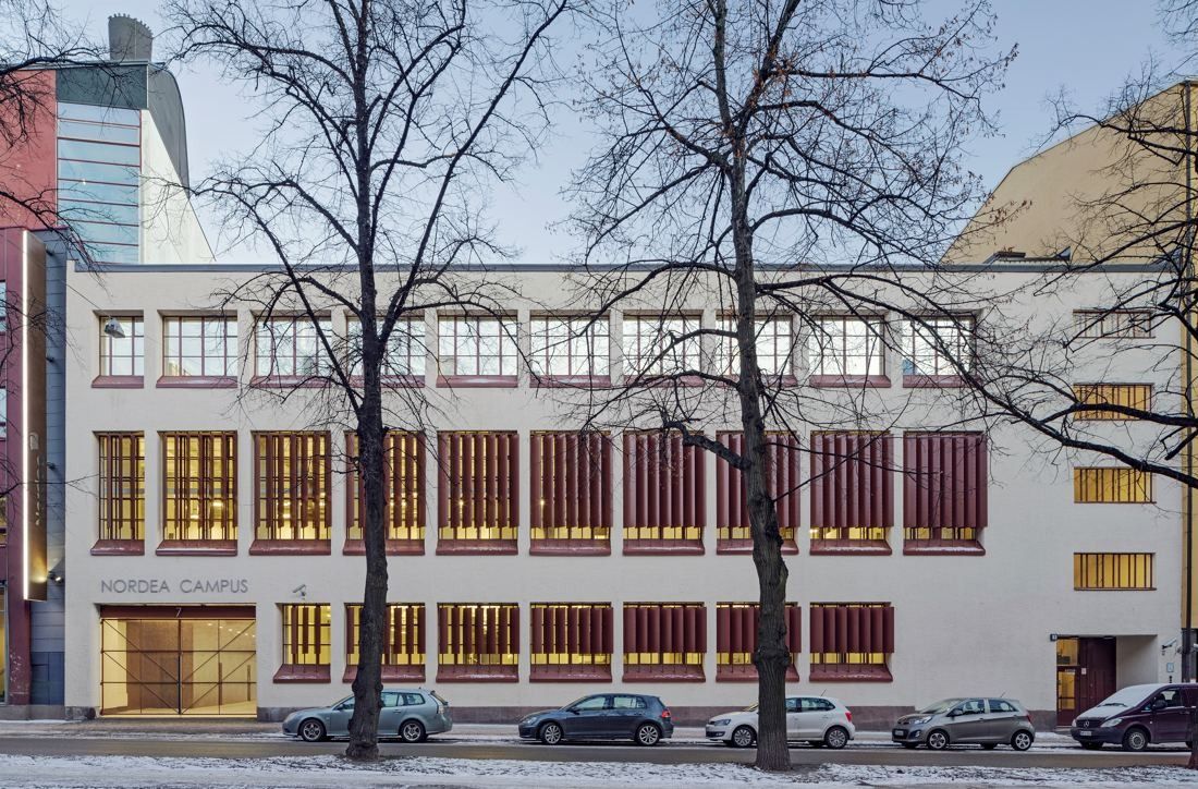 Nordea: Pale former factory building with rows of red-framed windows behind bare trees