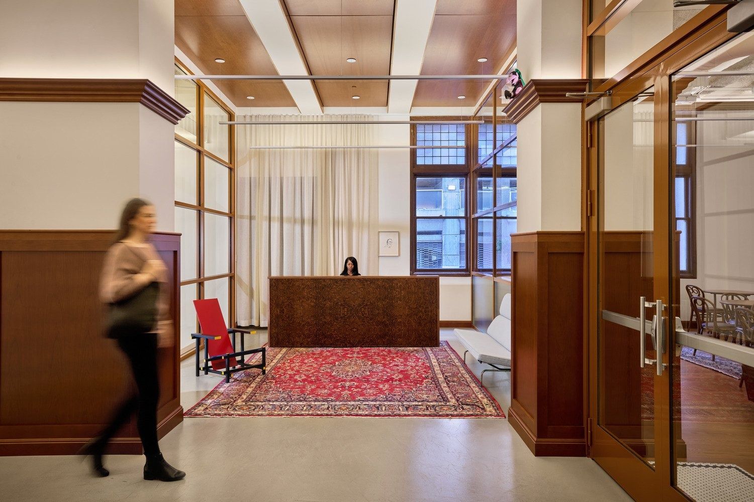 Notion: Entry with a carved wooden desk on a red Persian rug, coffered ceiling, glass doors and a red-and-blue chair