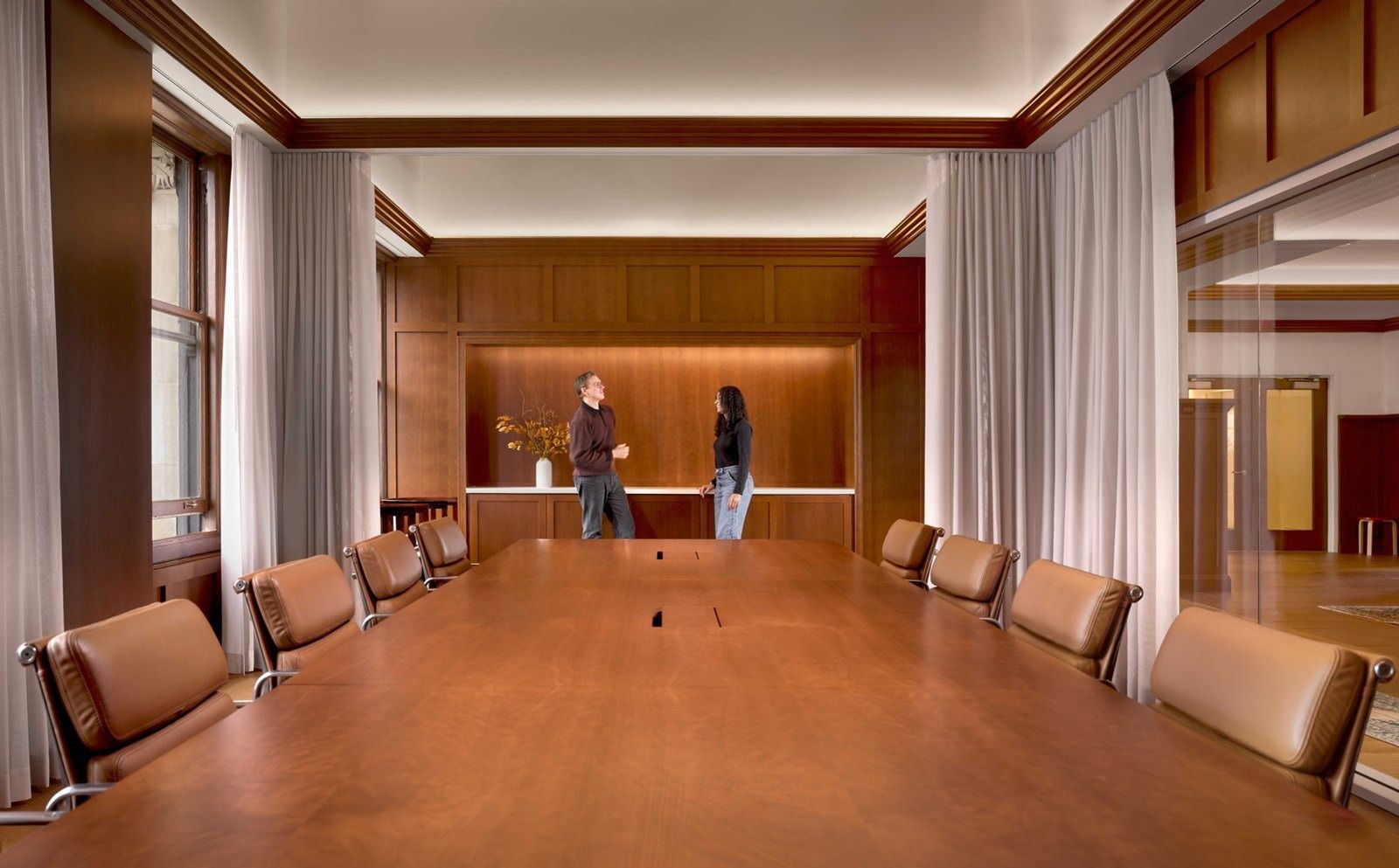 Notion: Long wooden table with leather chairs in a wood-paneled room framed by sheer curtains