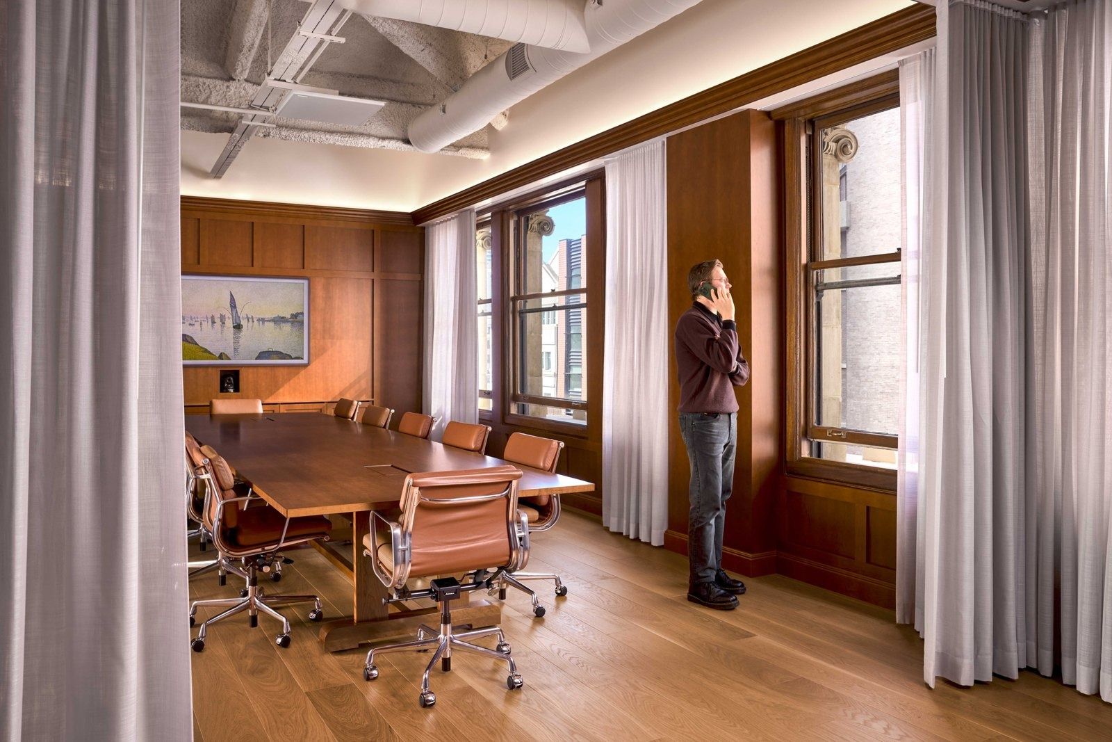 Notion: Wood-paneled room with a wooden table, leather chairs, a seascape painting and tall windows behind sheer curtains