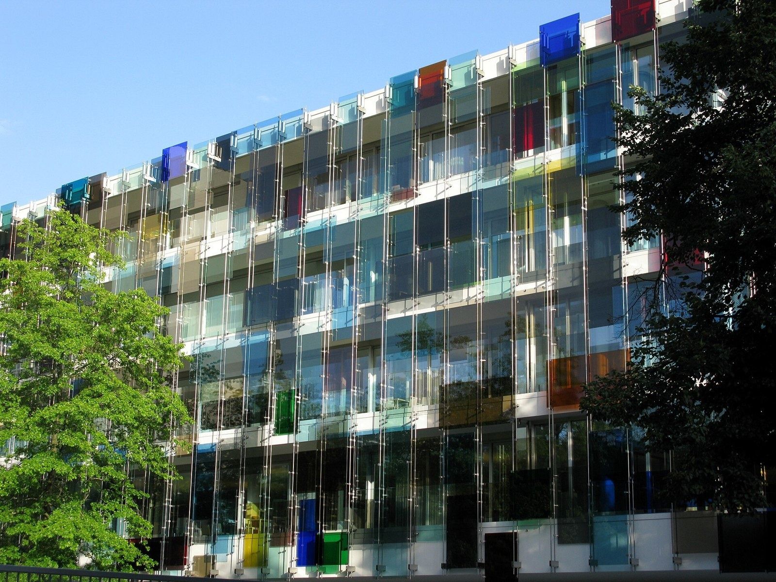 Novartis: Long façade of coloured glass panes behind trees