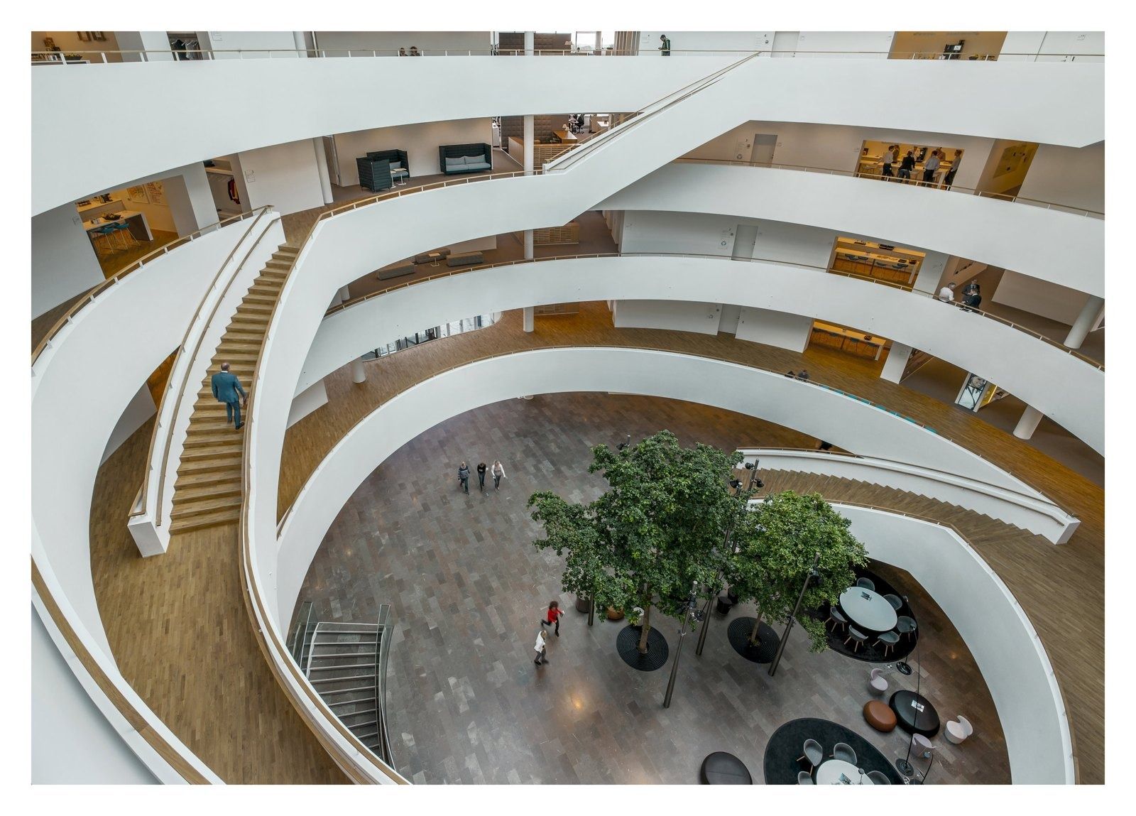 Curving white balconies spiral around an atrium with trees
