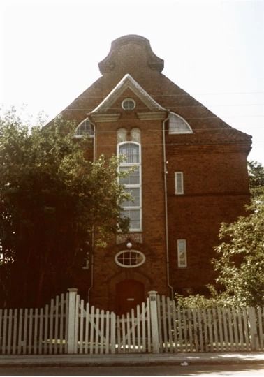 Faded colour photo of a tall red-brick villa behind a white picket fence