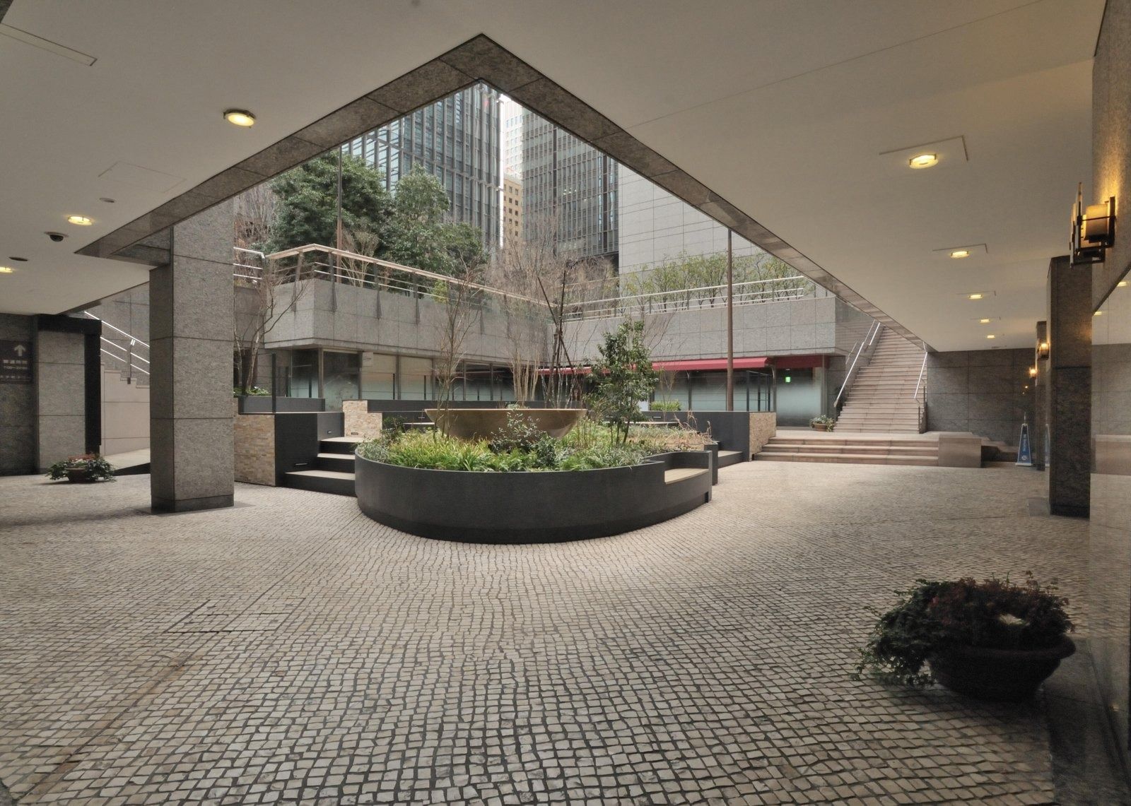 NTT: Covered plaza with a round planter under a pitched glass roof