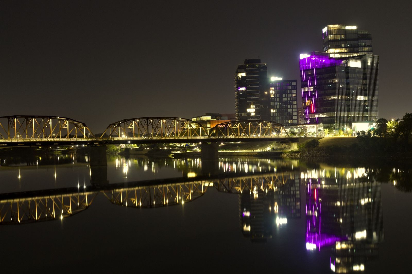Nutrien: A lit steel bridge and glowing towers reflected in a river at night