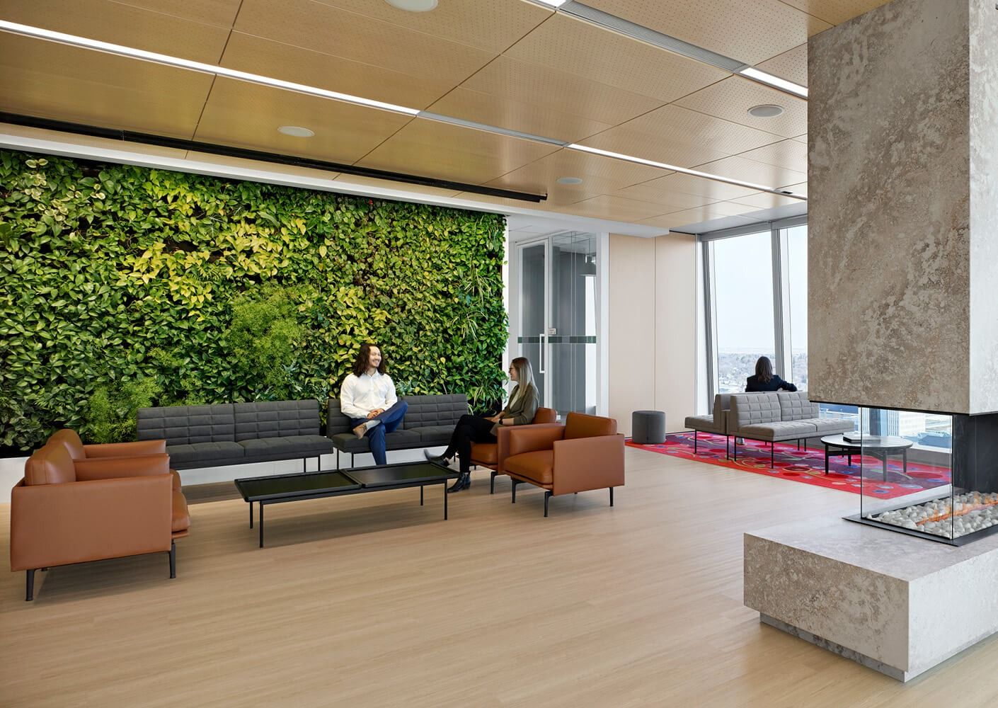 A lounge with leather chairs in front of a large green living wall and a stone fireplace