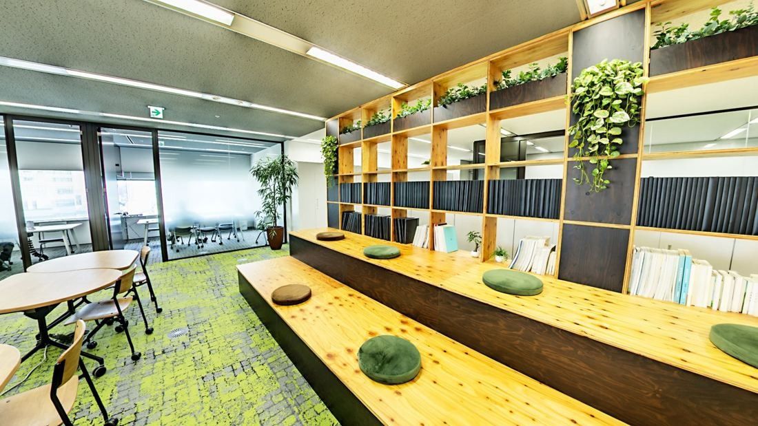 Obayashi: Lounge with wooden step seating, cushions, shelves and plants by the windows