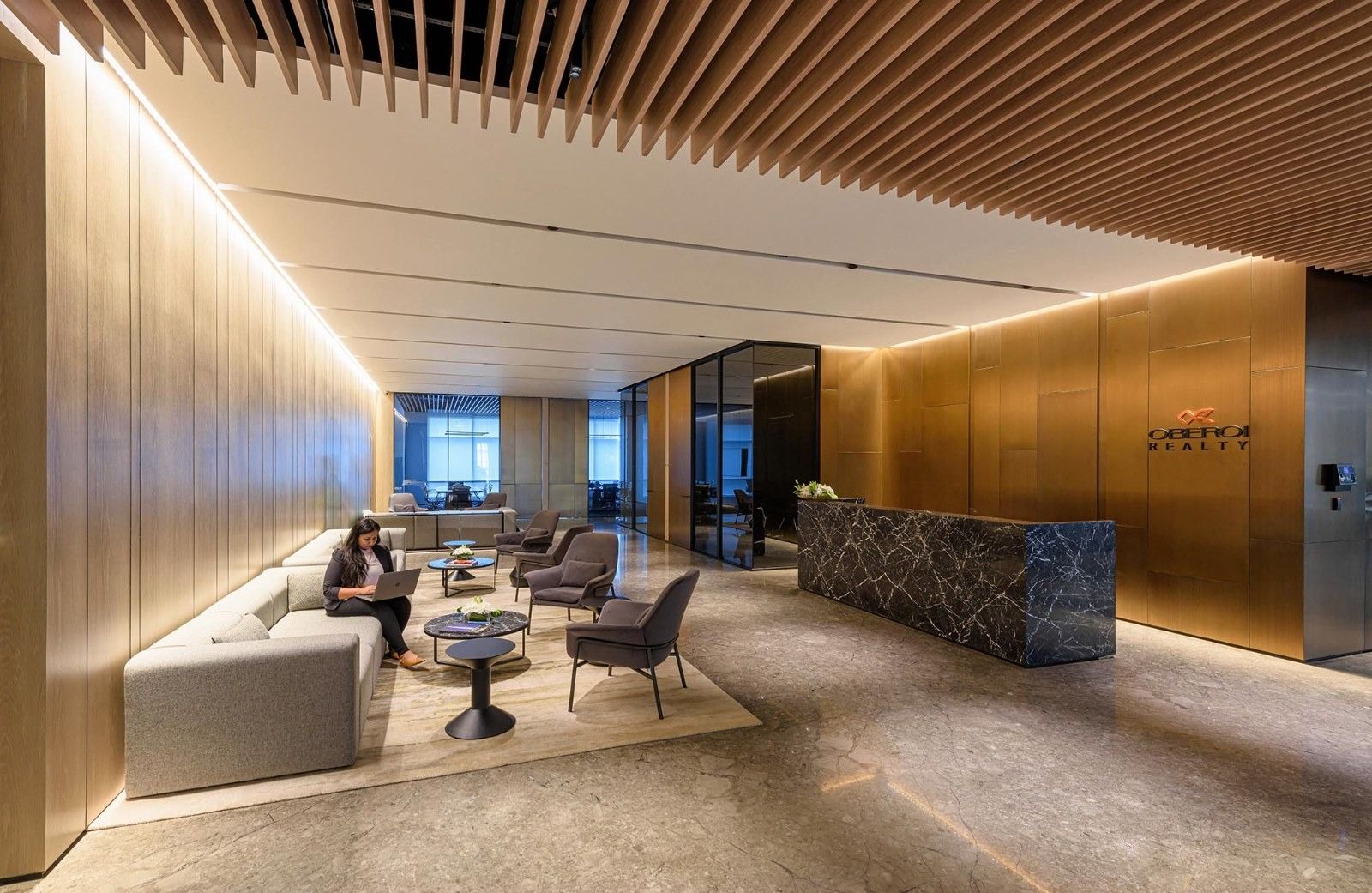 A lobby with a wooden slat ceiling, lounge chairs and a stone reception desk