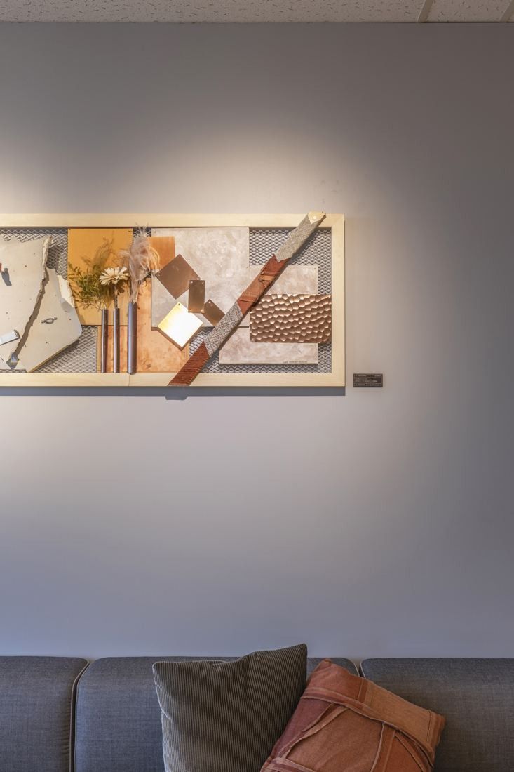 Okamura: Framed collage of materials on a grey wall above cushions