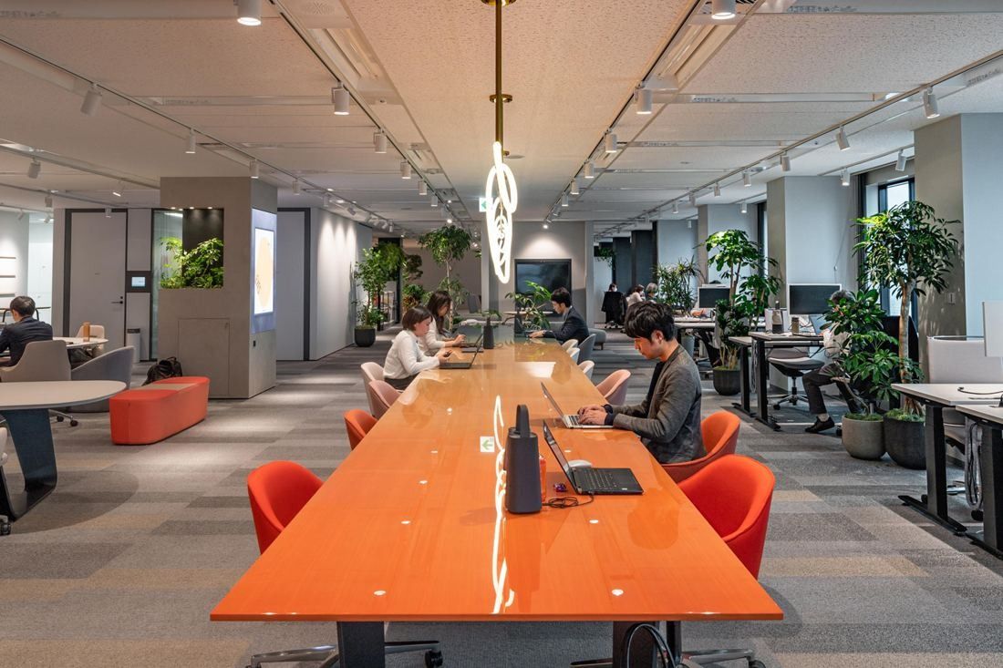 Okamura: Long glossy orange table with orange chairs running down an open office