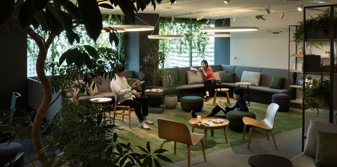 Okamura: Lounge with sofas, low tables, green carpet and indoor trees by the windows