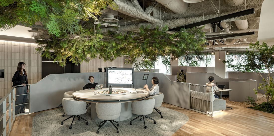 Okamura: Round white meeting table in a sunken area ringed by curved walls and plants