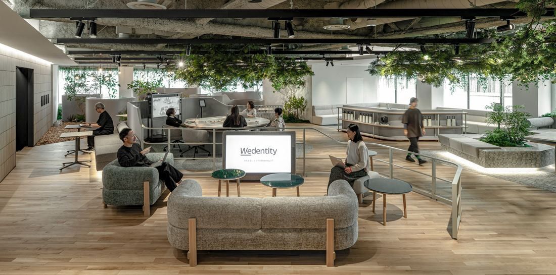 Okamura: Upholstered sofas and round tables along a path with greenery overhead