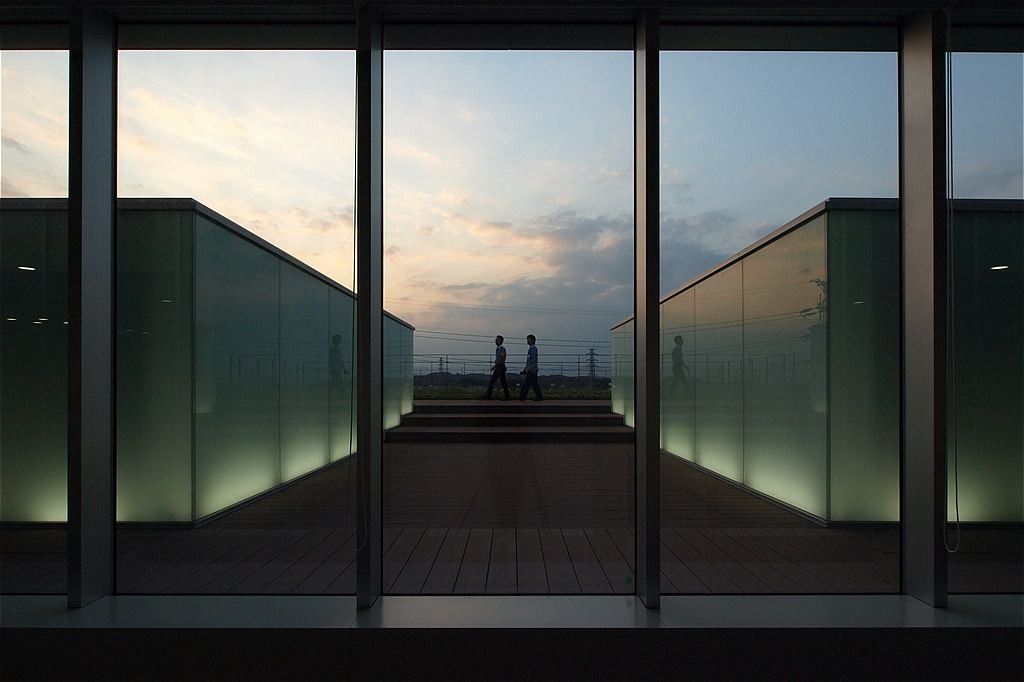 Olympus: Glass doors opening onto a roof terrace at dusk with two distant silhouettes