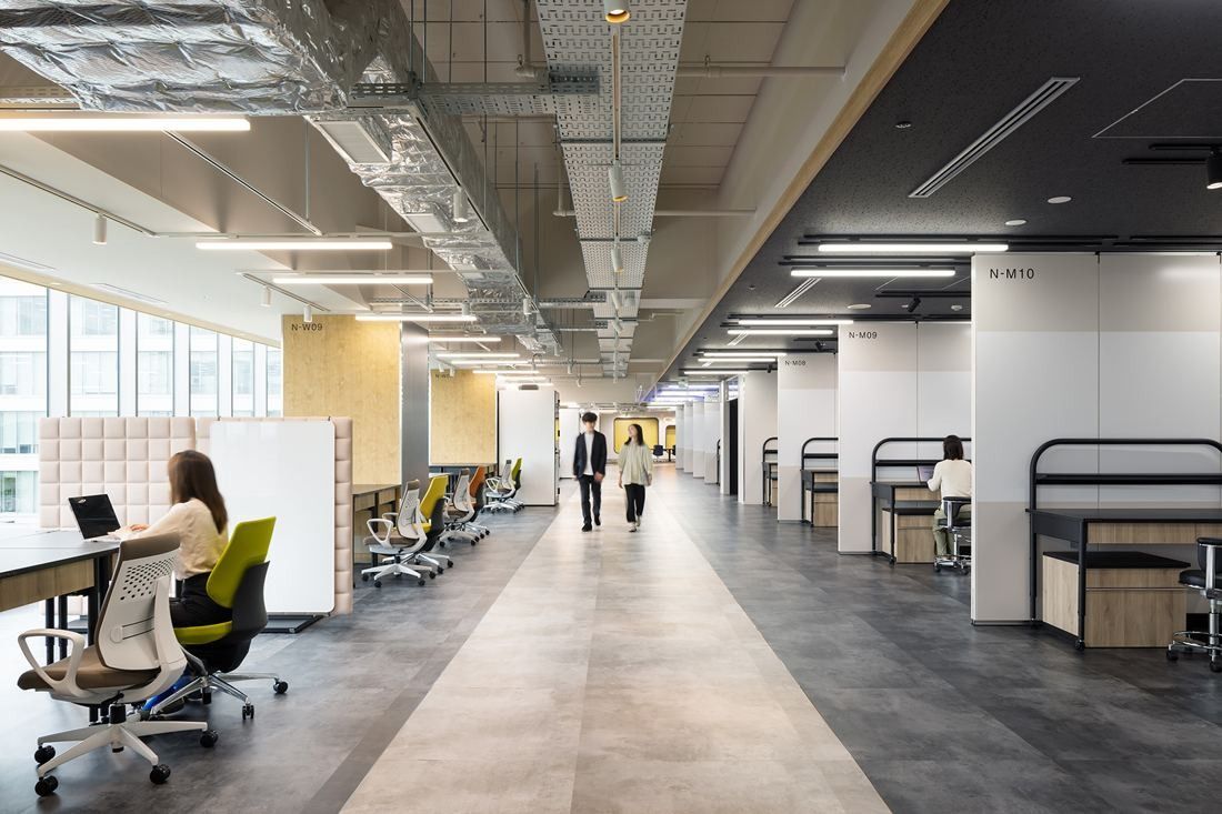Olympus: Long aisle between desks and white partitioned lab bays under an exposed ceiling