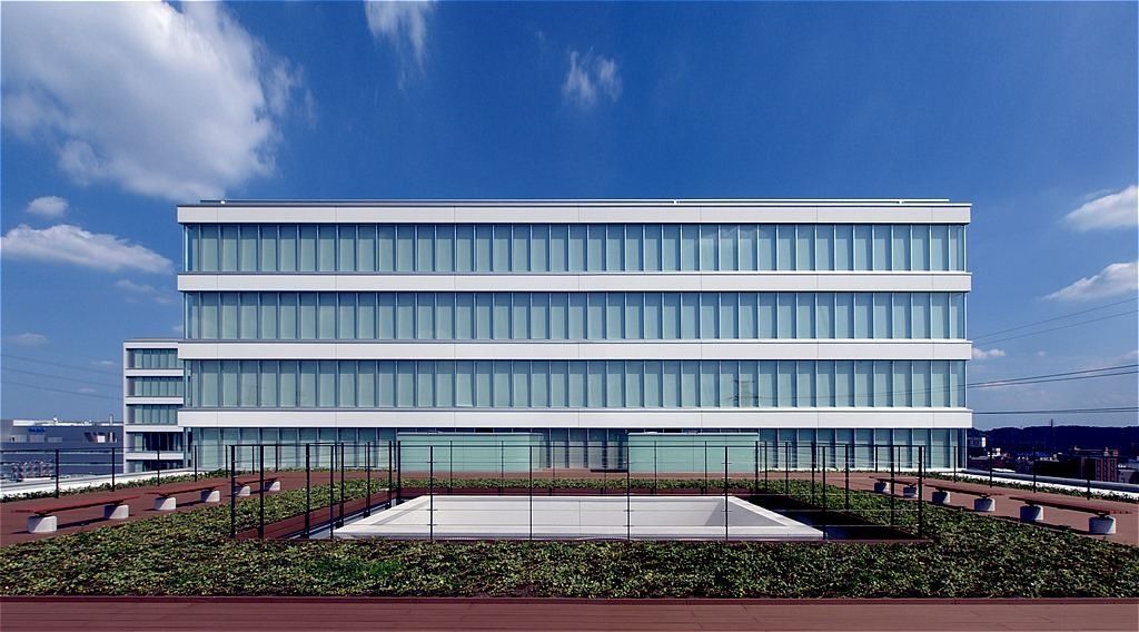 Olympus: Long low glass façade seen across a green roof garden