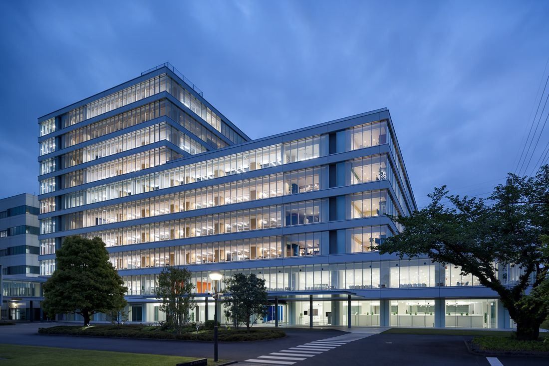 Multi-storey glass office building lit at dusk, with trees in front