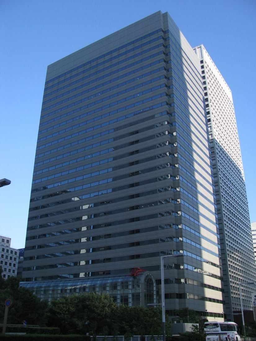 Tall dark glass office tower seen from the street under a blue sky
