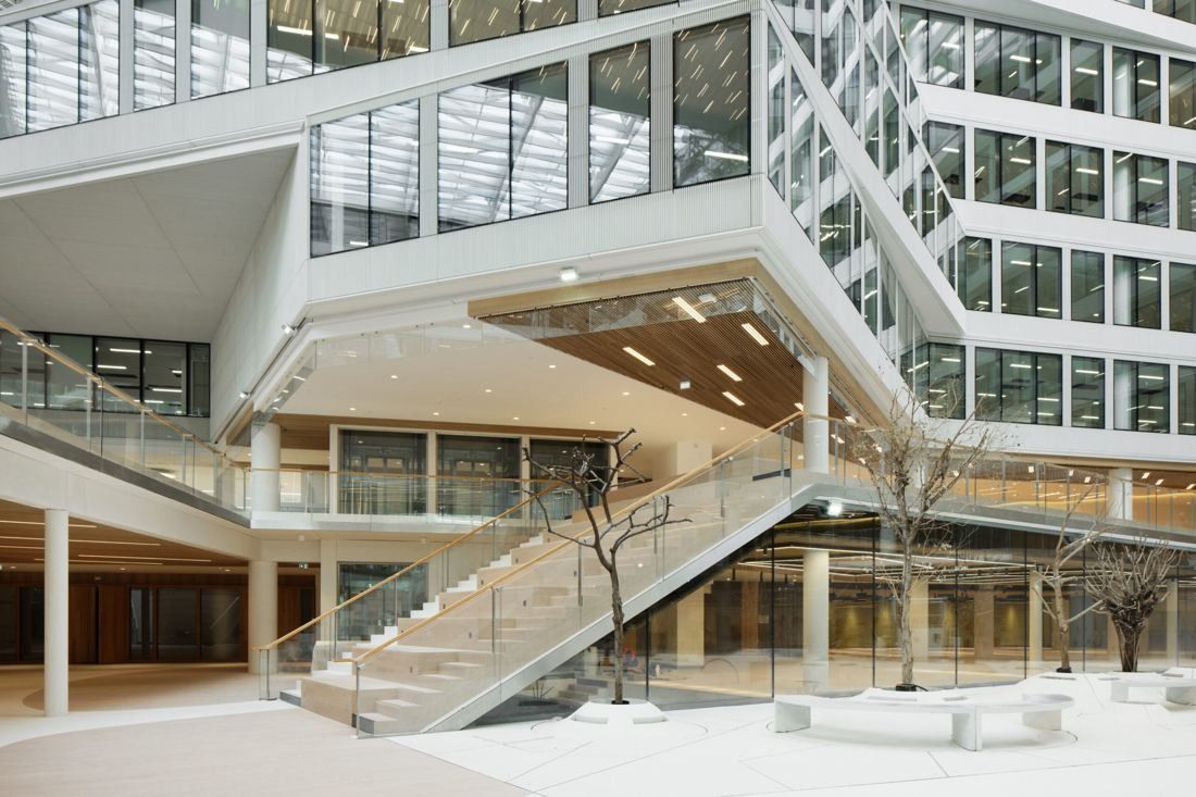 Orange: Atrium with a broad staircase, slim columns and young trees under a suspended white volume