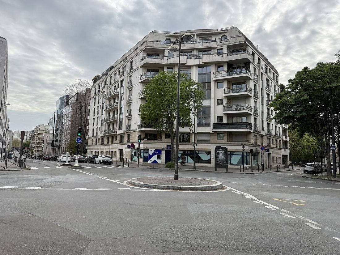 Corner of a city square with a curved white apartment building, trees and a small central island