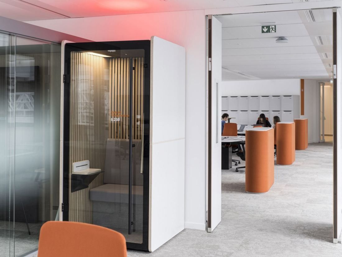 Orange: Glass phone booth with a seat beside an open office with orange high tables and lockers