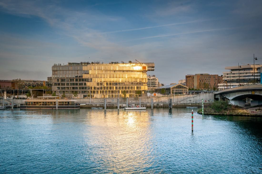 Orange: Low glass building catching the evening sun on the far bank of a wide river, with a bridge to the right