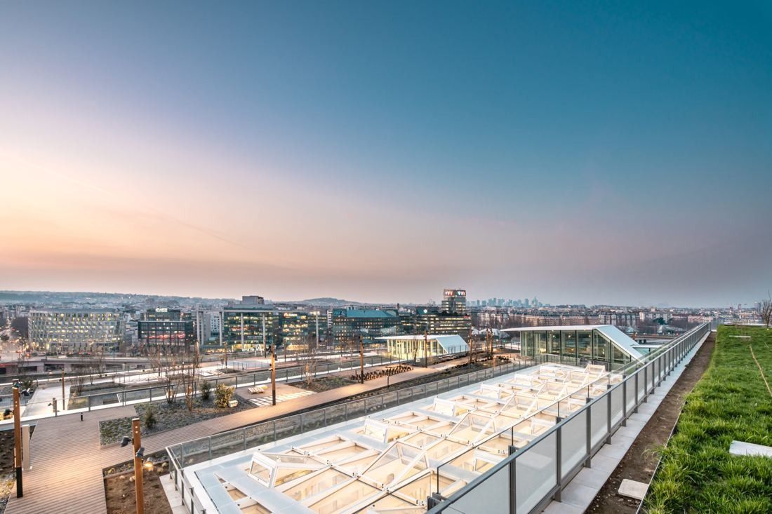Orange: Planted roof terrace with a long glass roof, overlooking the city at dusk