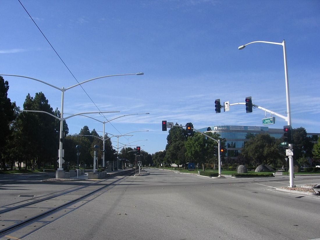 Wide suburban road with light-rail poles, traffic lights and low office buildings