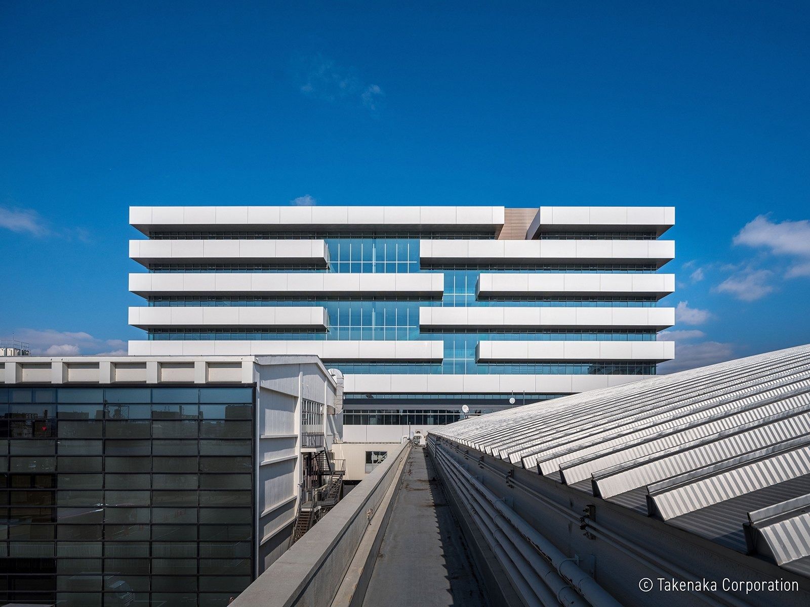 Panasonic: Front of a white building with stacked horizontal floors seen across low roofs