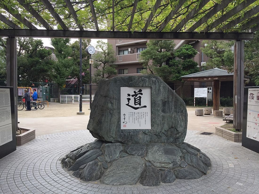 Large stone monument engraved with a single kanji under a pergola in a small park