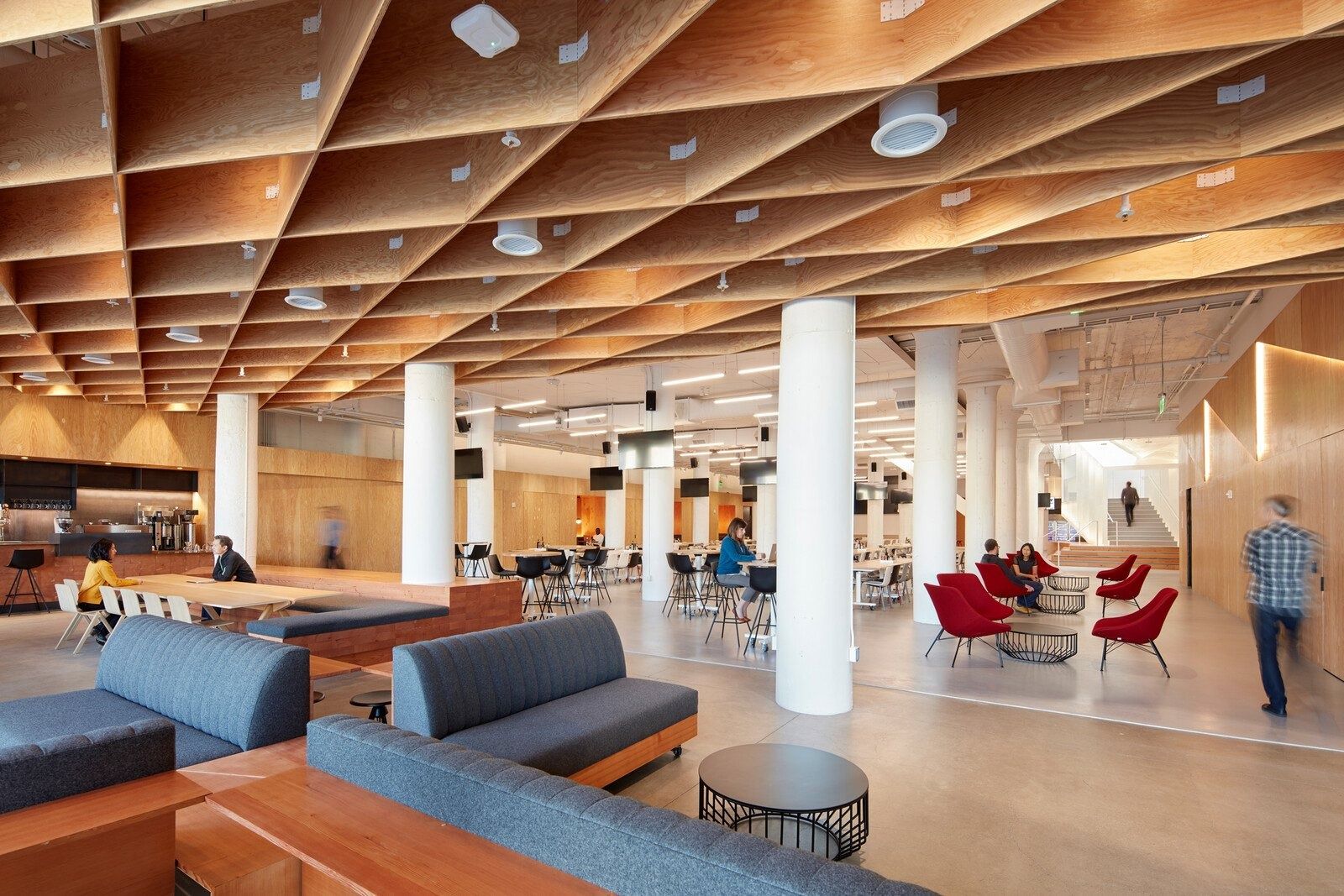 An open floor under a deep timber coffered ceiling with sofas and red chairs