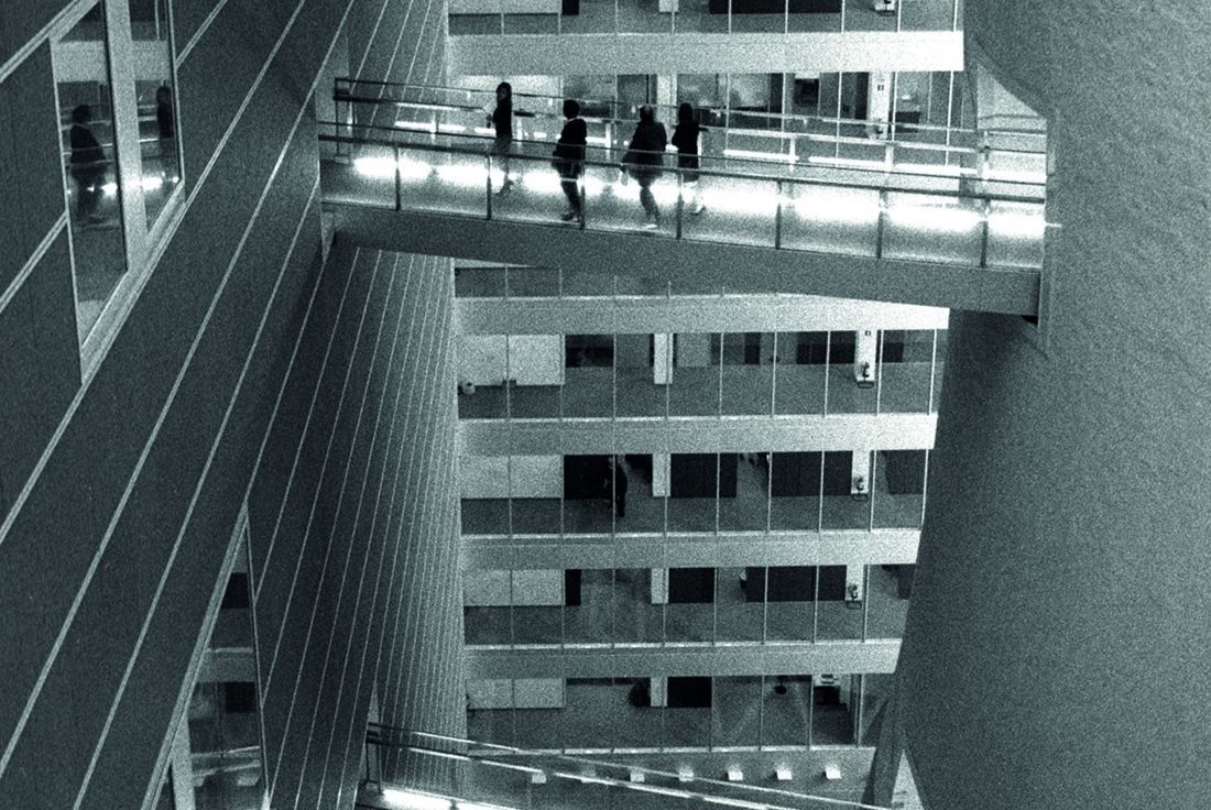 Pirelli: Black-and-white view of silhouetted people crossing a glazed walkway between office floors and the tower
