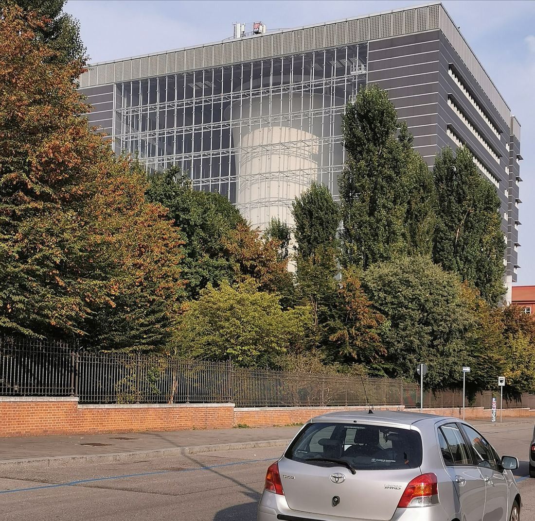 Pirelli: Grey office block with a glass façade revealing a tower inside, seen from a tree-lined street
