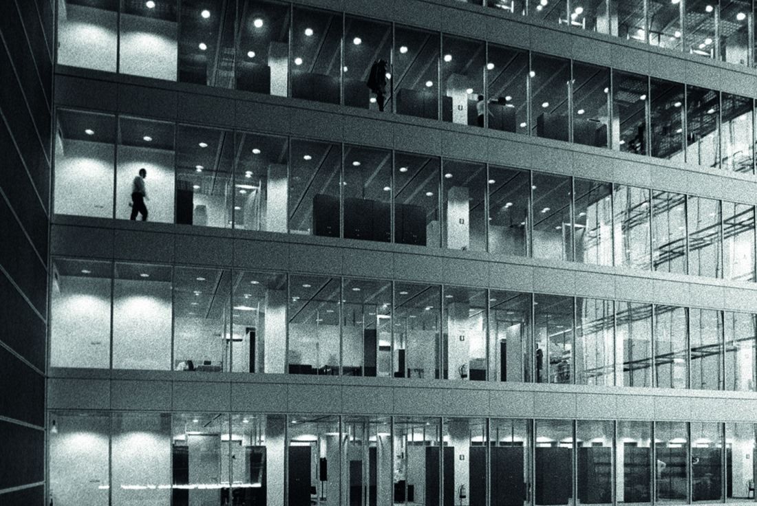 Pirelli: Lit office floors seen through a glass façade at night with a few distant figures
