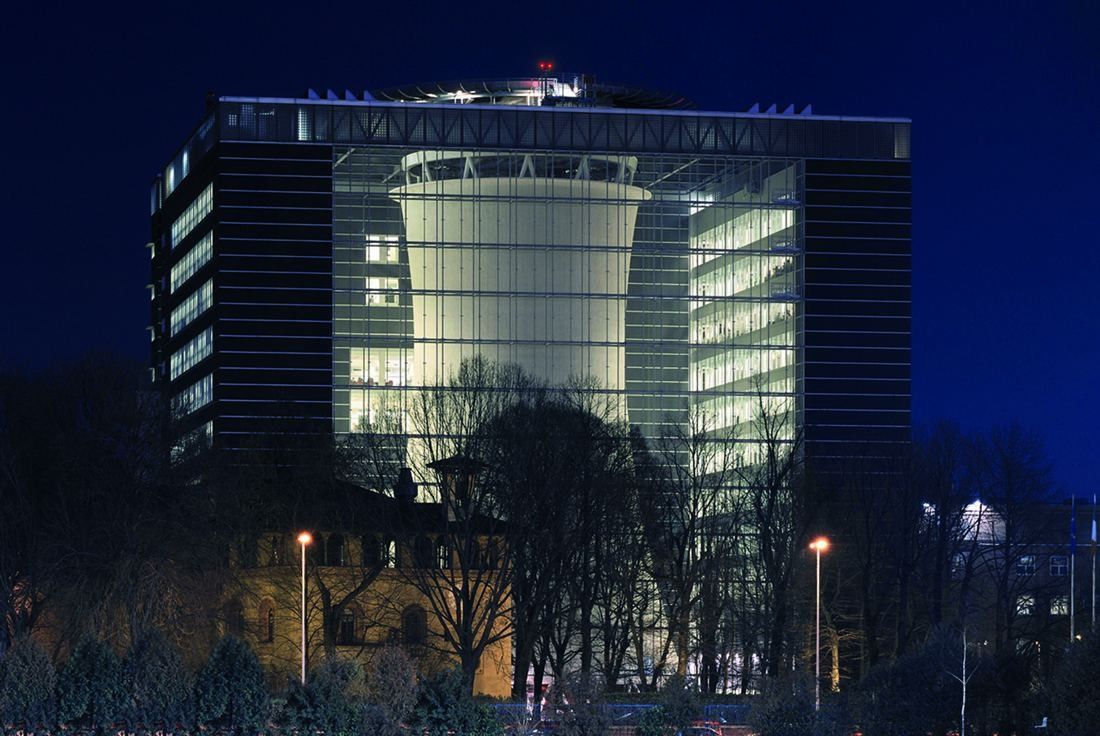 Office building at dusk with a lit cooling tower visible behind a full-height glass wall