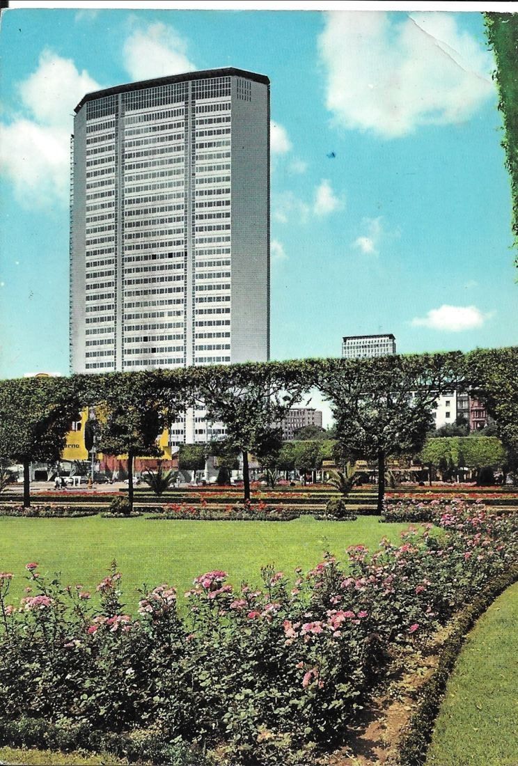 Slender glass tower rising behind a flower garden in a colour postcard