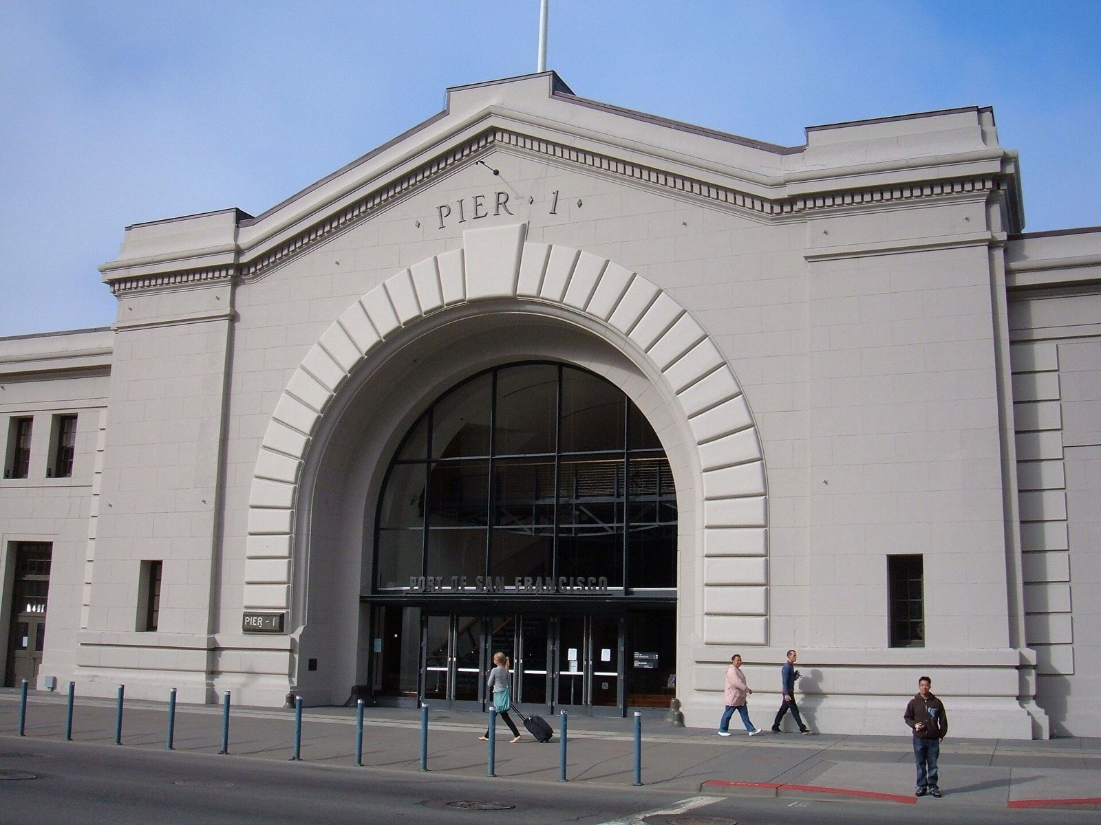 A white historic pier building with a large arched glass entrance and the words Pier 1