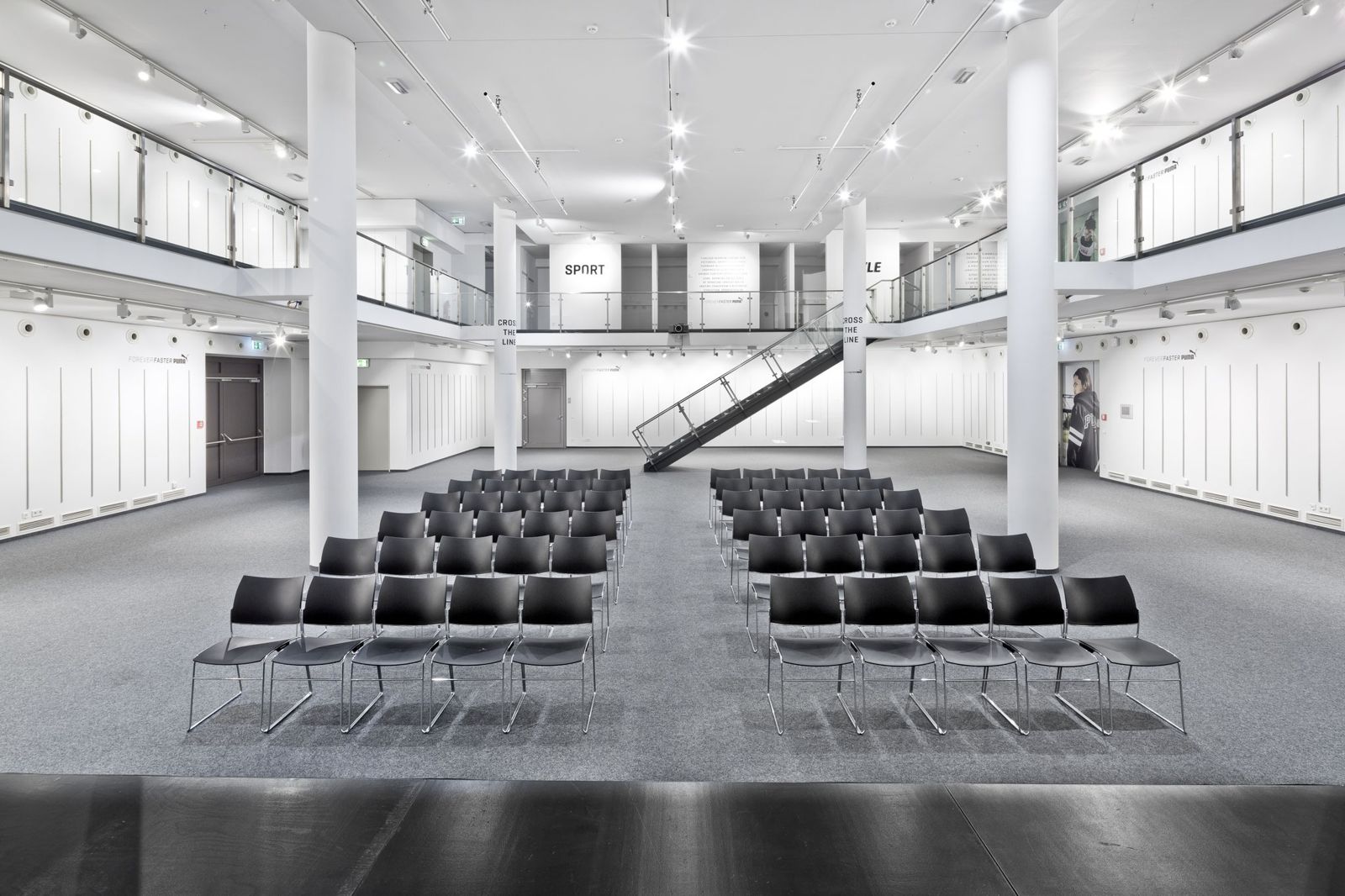 PUMA: White event hall with rows of chairs and a gallery