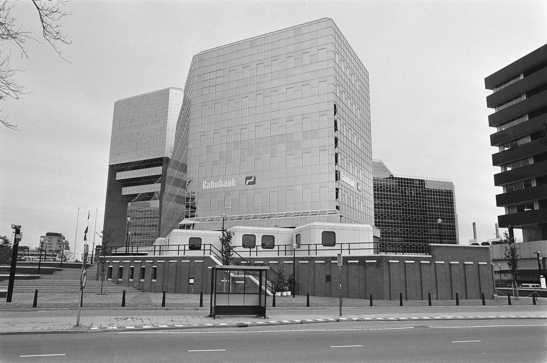 Black-and-white photo of a large angular office building with a grid facade beside a wide street