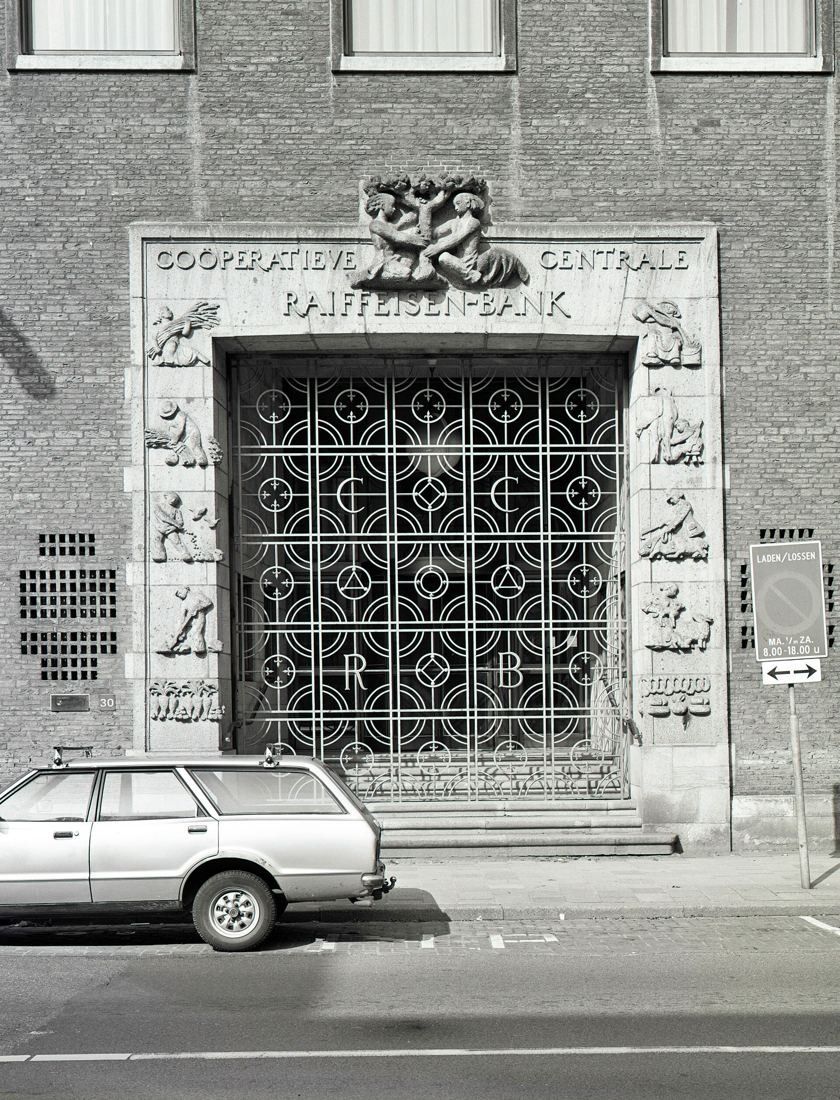 Black-and-white photo of a stone-framed entrance with relief sculpture and a decorative metal grille door